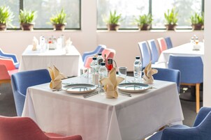 Un comedor con mesas dispuestas para dos, cada una con platos, cubiertos y botellas de agua.
