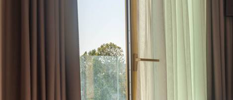 A bedroom with a bed, a sliding glass door leading to a balcony, and curtains.