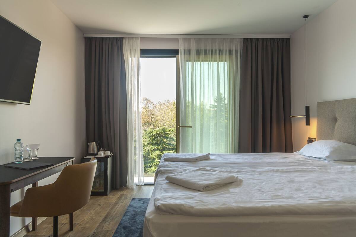 Ein Hotelzimmer mit Bett, Schreibtisch, Stuhl und Blick auf Grünflächen.