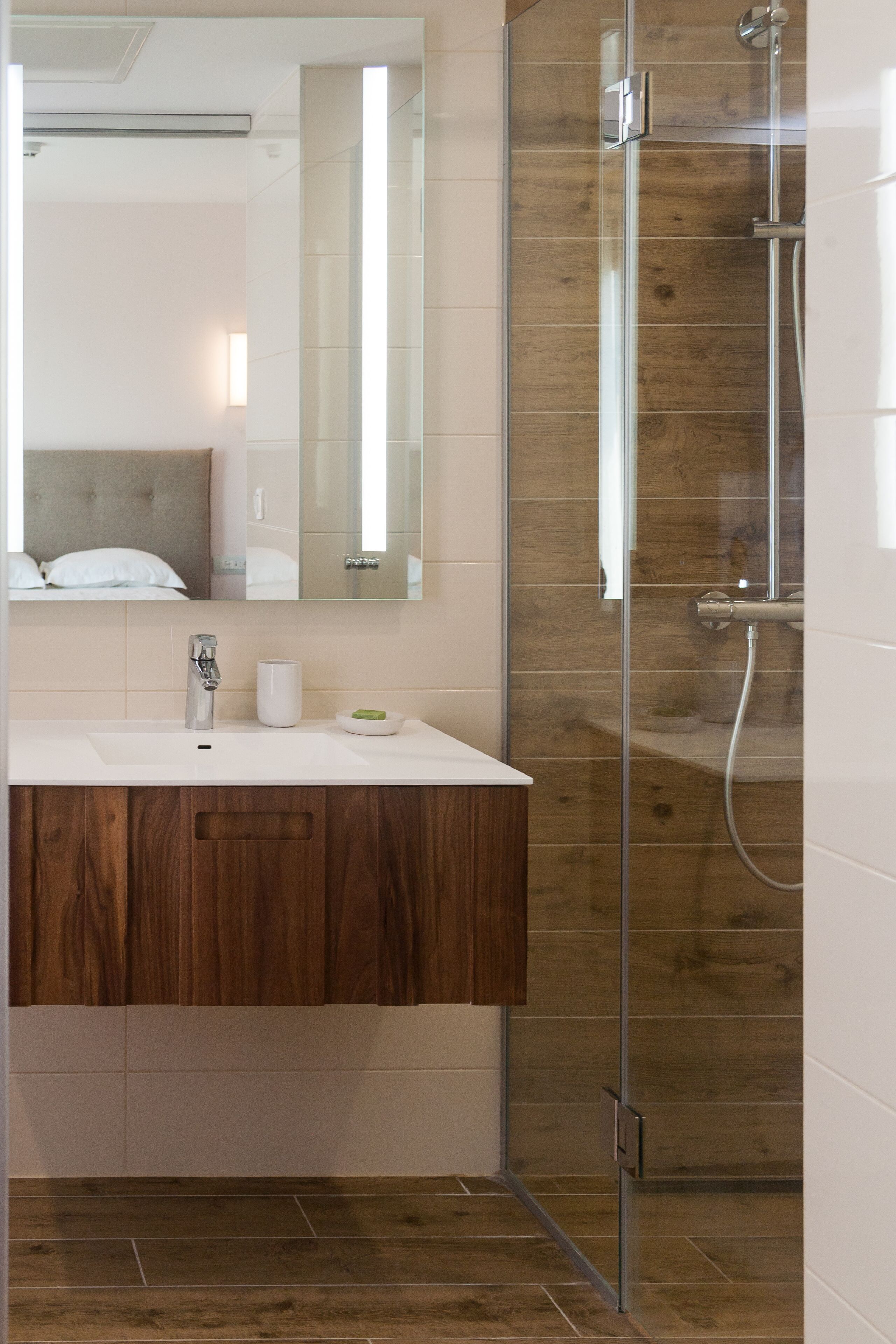 Un baño moderno con tocador de madera, cabina de ducha con mampara de vidrio y un espejo grande.