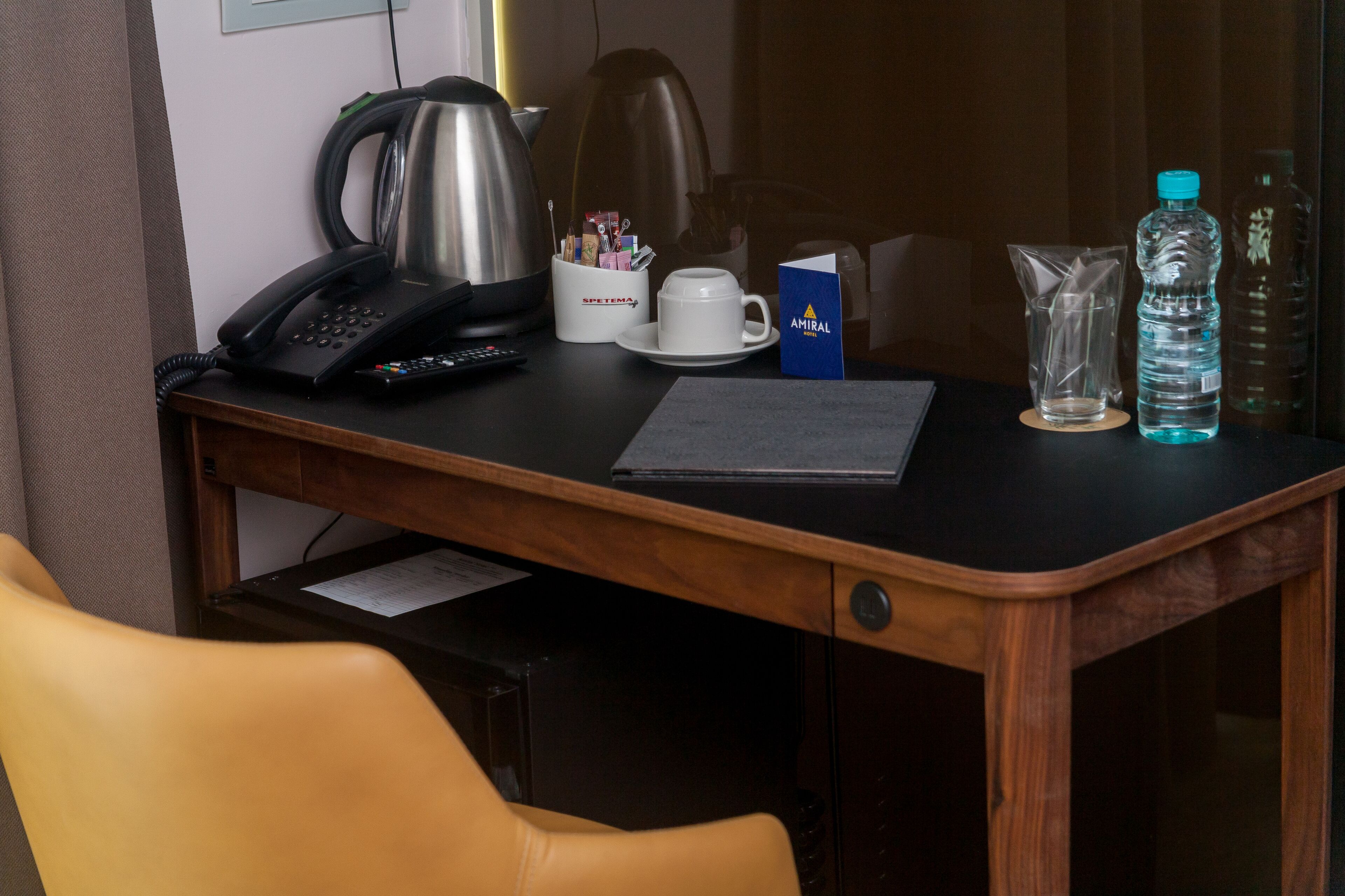 A hotel desk with a telephone, a coffee maker, a cup, a water bottle, and a room key.