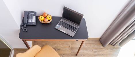 A room with a desk, a laptop, a telephone, and a fruit basket.