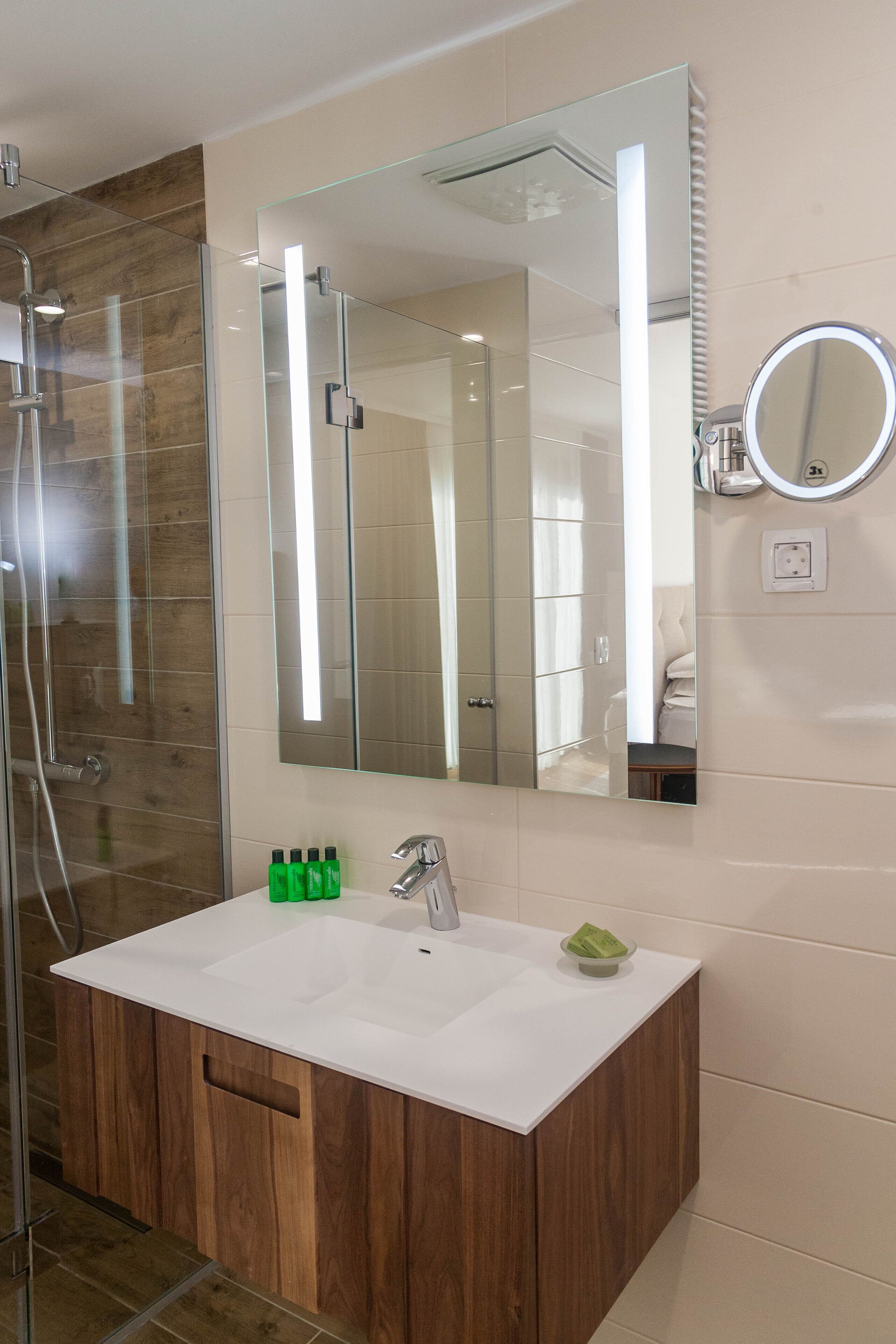 Un baño con cabina de ducha de vidrio, un espejo grande, un lavabo blanco y un mueble de tocador de madera.