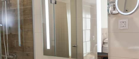 A bathroom with a glass shower enclosure, a large mirror, a white sink, and a wooden vanity.
