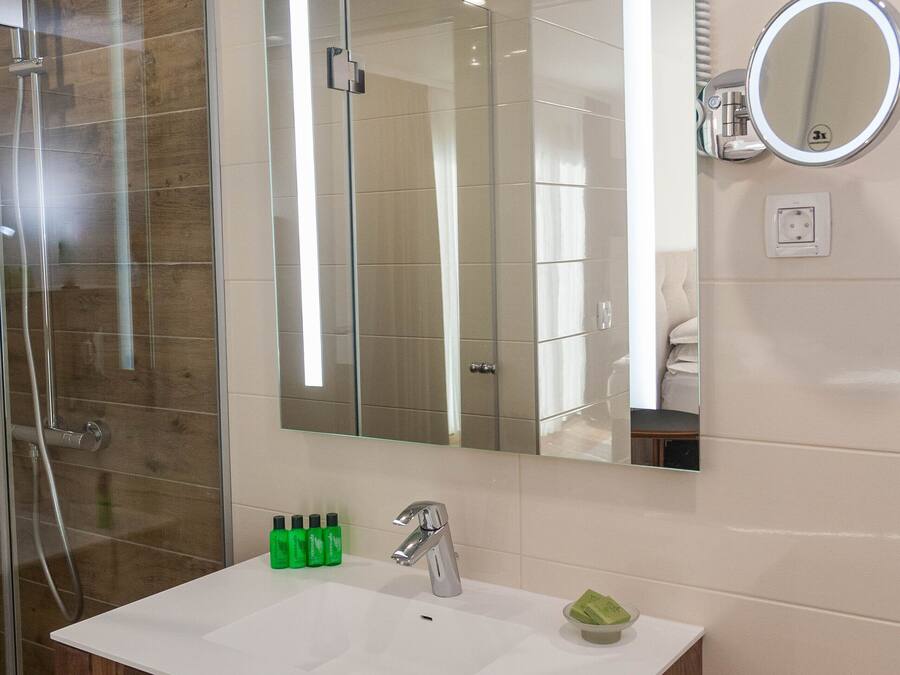 Un baño con cabina de ducha de vidrio, un espejo grande, un lavabo blanco y un mueble de tocador de madera.