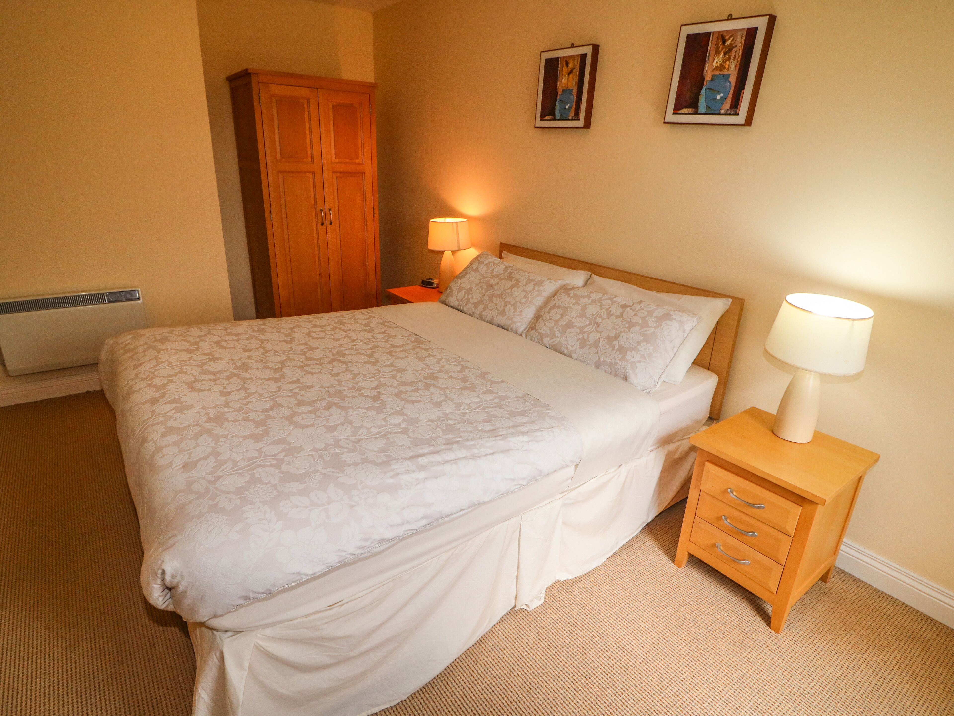 A neatly made bed with a floral bedspread, a bedside lamp, and a wooden nightstand with drawers.