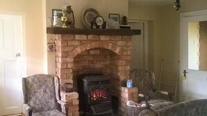 A living room with a brick fireplace, two patterned armchairs, a sofa, and a mantelpiece with decorative items. - Ferrys (Portsalon)