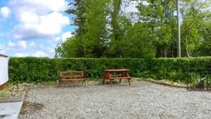 A gravel area with a bench and picnic table, surrounded by greenery and a hedge. - Ferrys (Portsalon)