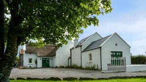 A white building with a green door and a white fence. - Annie's Cottage (Clogher)