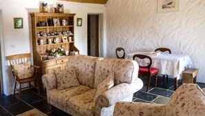 A cozy room with a floral sofa, a wooden cabinet with kitchenware, a dining table with chairs, and a framed picture on the wall. - Annie's Cottage (Clogher)
