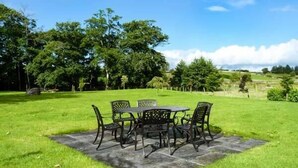 A patio with a table and chairs, surrounded by a grassy lawn and trees. - Annie's Cottage (Clogher)