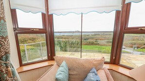 A corner room with a cushioned seating area, large windows, and a view of the countryside. - Starbay House (Eyeries)