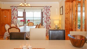 A dining area with a table set for four, chairs, a wooden bowl, and a view of the outdoors through large windows. - Starbay House (Eyeries)