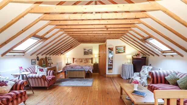 Een gezellig zolderkamer met houten balken, een bed, twee banken, een tafel en een stoel.