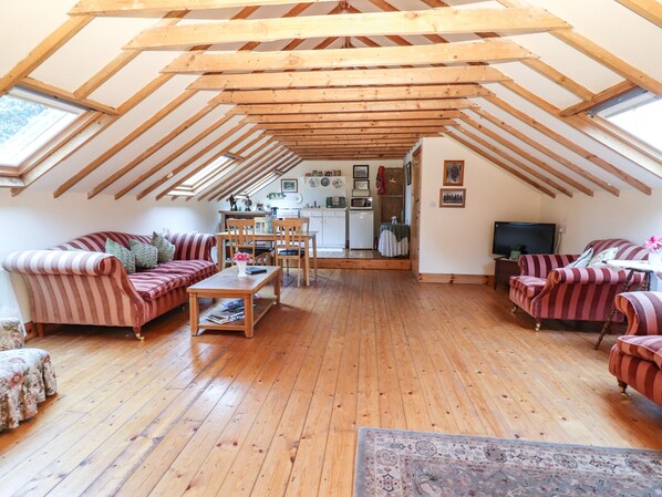 A cozy attic room with wooden beams, a dining area, and a kitchen. - Mrs Delaney's Loft (Ardfinnan)