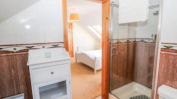 Un baño con ducha, inodoro y una mesita de noche con lámpara.