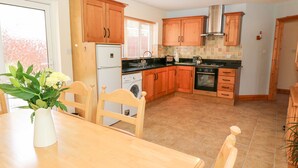 A kitchen with wooden cabinets, a refrigerator, a washing machine, and a stove. - The Blue Annex (Tralee)