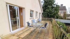 Une terrasse en bois avec une porte vitrée donnant sur une pièce, une table ronde avec des chaises et un petit espace extérieur aménagé avec des sièges.