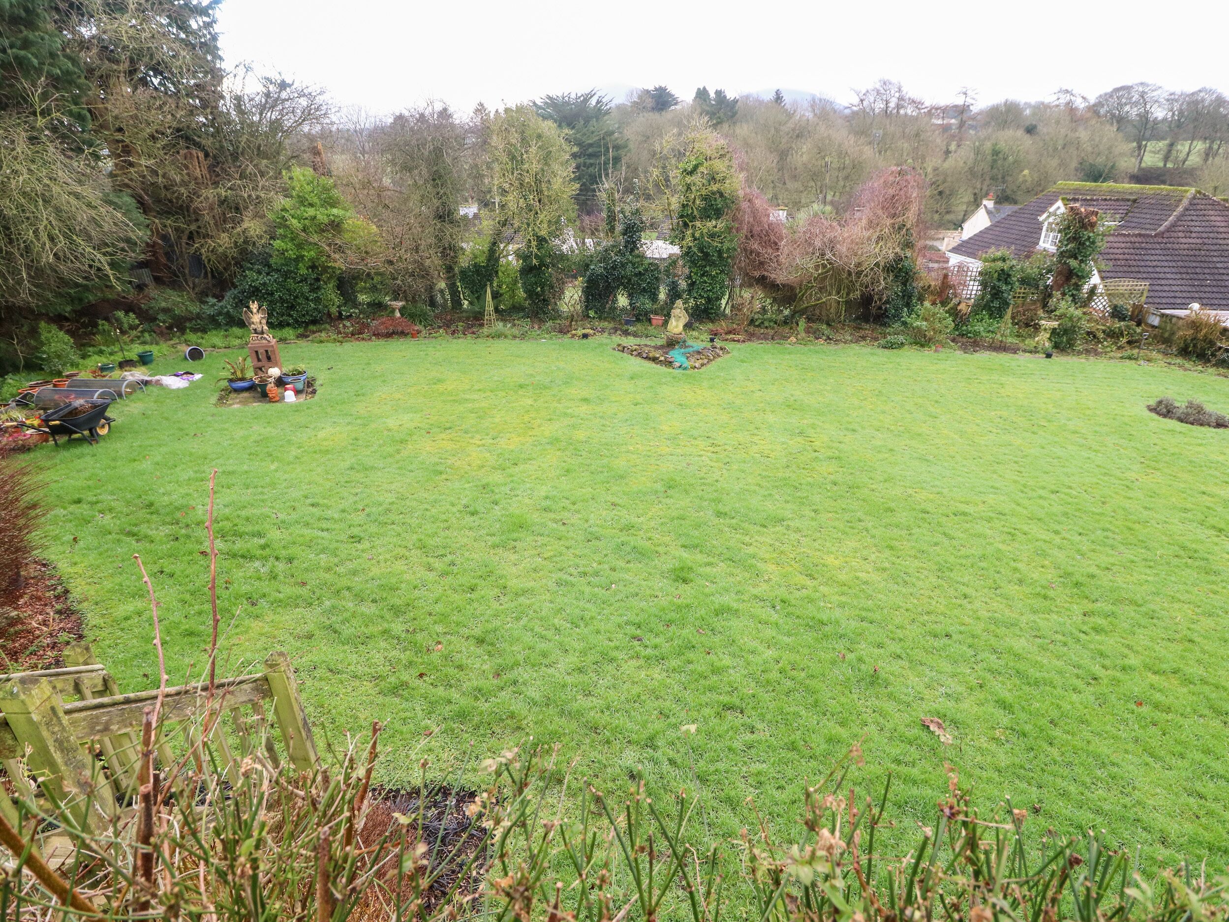 A spacious backyard with a lawn, a small garden area with potted plants, and a wooden play structure.