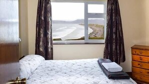 Un dormitorio con cama, ventana con vista a la playa y cómoda de madera.