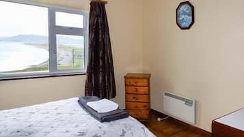 Un dormitorio con cama, cómoda, radiador y ventana con vista al mar.