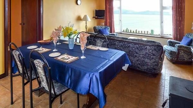 Un comedor con una mesa dispuesta para cuatro personas, un sofá y vista al mar.