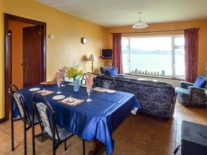 Un coin repas avec une table dressée pour quatre personnes, un canapé et une vue sur la mer.