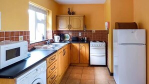 Una cocina compacta con armarios de madera, un microondas, una estufa y una lavadora.