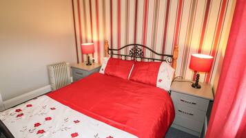 Ein ordentlich bezogenes Bett mit einer rot-weißen Blumenbettdecke, zwei Nachttischlampen, einem Holzkopfteil und einem gestreiften Wandhintergrund.