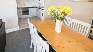 A dining area with a wooden table, white chairs, and a vase of yellow flowers. - Island View (Ardmore)