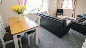 A living room with a wooden dining table, a black leather sofa, and a TV on a stand. - Island View (Ardmore)