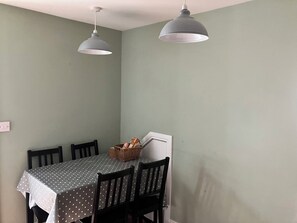 A dining area with a table covered in a polka dot tablecloth, four chairs, two pendant lights, and a basket of bread on the table. - Silver Birch House (Dunloe Upper)