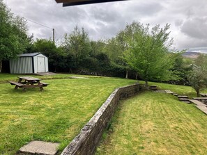 A grassy backyard with a picnic table, a shed, and a stone wall.