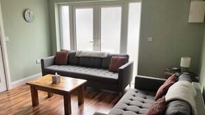 A living room with a sofa, a coffee table, and a window with blinds. - Silver Birch House (Carhoonahone)