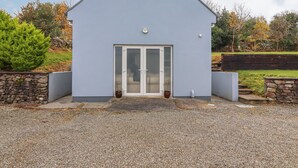 A modern building with a white exterior, a large glass door, and a stone wall on one side. - Silver Birch House (Carhoonahone)