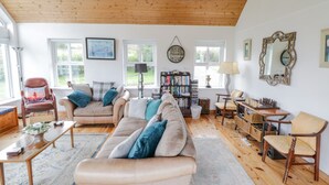 A spacious living room with a high wooden ceiling, a large sofa, a bookshelf, and a chess table. - Ben View (Renvyle)