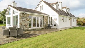 A modern house with a stone facade, large windows, and a patio with outdoor furniture. - Ben View (Renvyle)