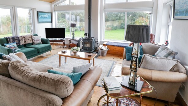 A spacious living room with a high ceiling, large windows, a fireplace, and comfortable seating. - Ben View (Renvyle)