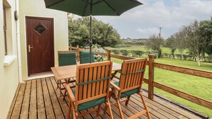 An outdoor wooden deck with a table and chairs, a green umbrella, and a view of a green landscape. - Silver Birch (Creegh)