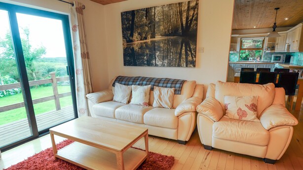 A living room with a sofa, a coffee table, and a large window with a view of greenery. - Silver Birch (Creegh)