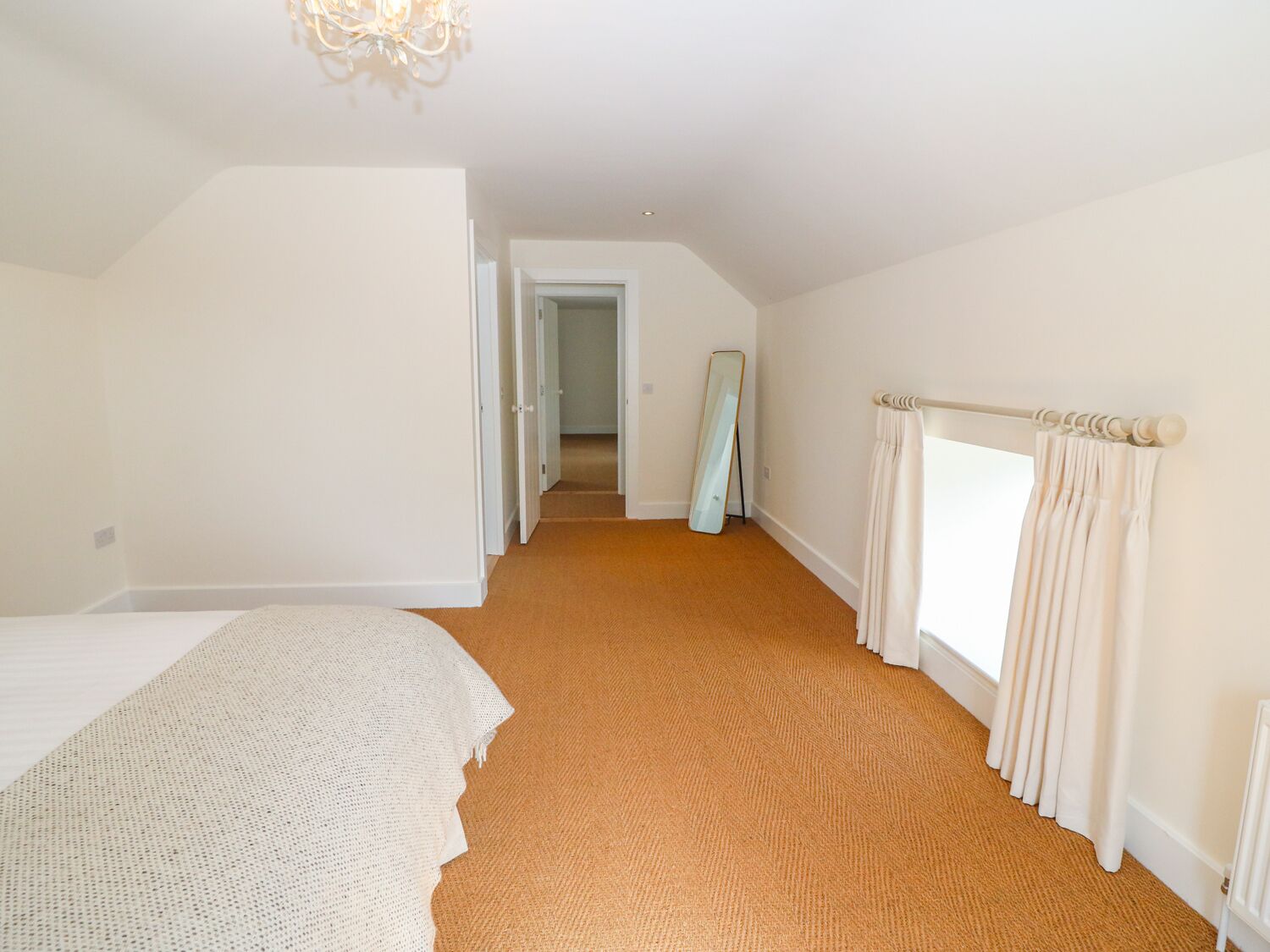 A bedroom with a large bed, a carpeted floor, a window with curtains, and a mirror leaning against the wall.