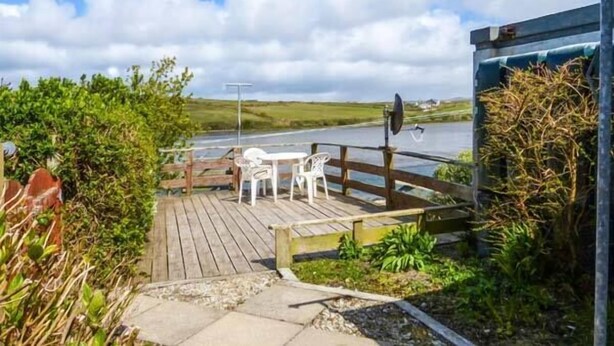 A wooden deck with outdoor seating, overlooking a body of water and a rural landscape.