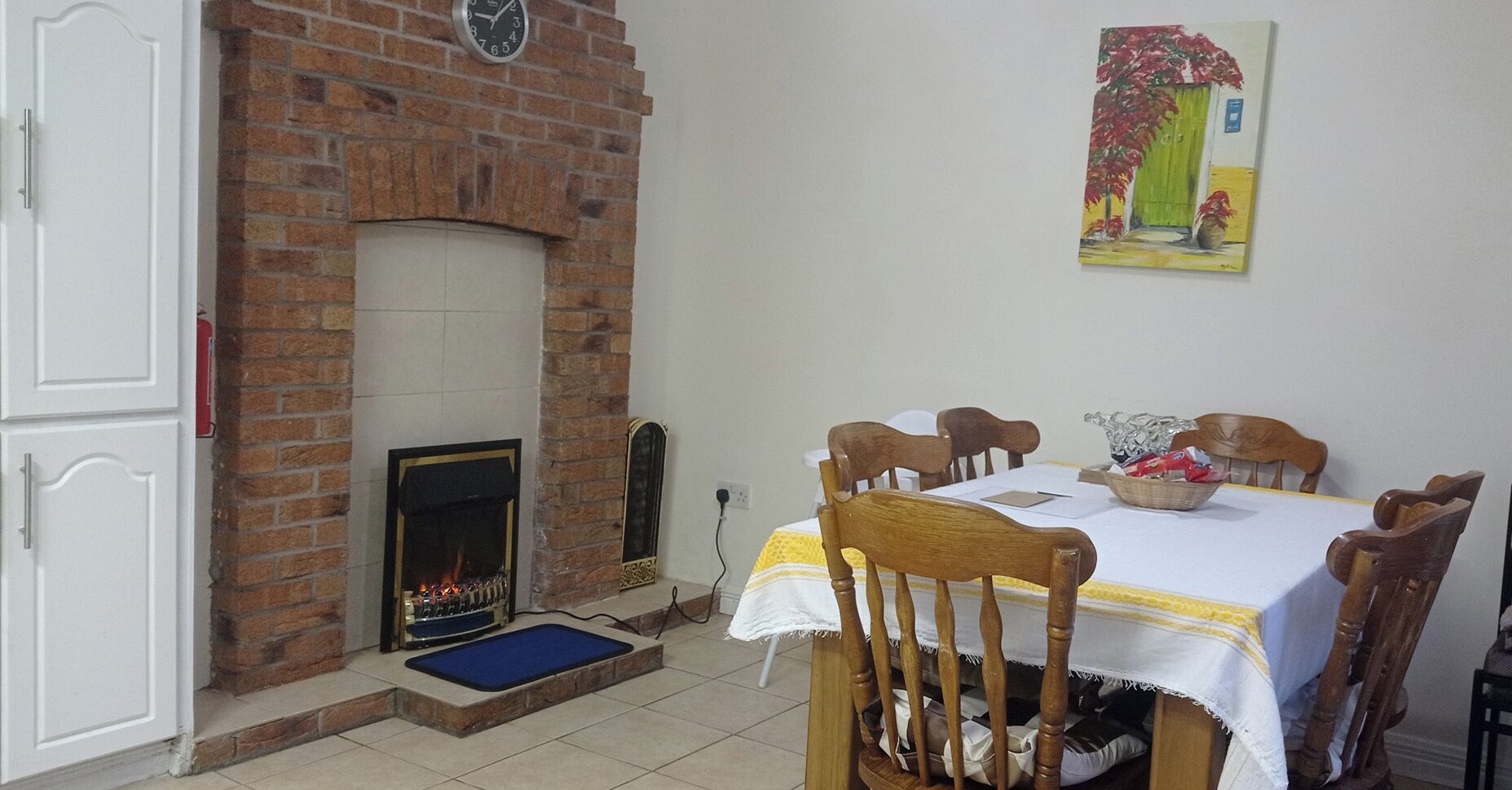 A dining area with a brick fireplace, a table with chairs, and a painting on the wall.