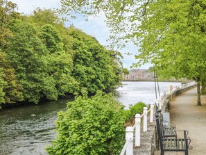 A riverside walkway with a stone railing, benches, and lush greenery. - Gapple Cottage (Rathmullan)