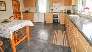 Una cocina compacta con armarios de madera, una mesa de comedor con mantel estampado de peces, un refrigerador, un horno y una ventana con cortinas.