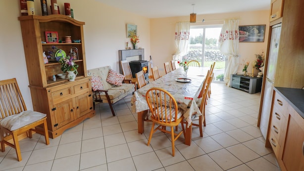 A cozy living room with a fireplace, wooden furniture, and a dining area with a tiled floor. - Lough Mask Road Fishing Lodge (Cong)