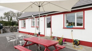 A red picnic table with a canopy, white chairs, and potted plants near a building with red trim and windows. - Lough Mask Road Fishing Lodge (Cong)