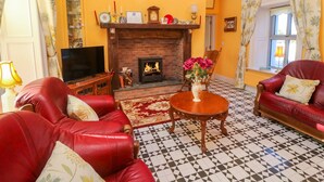 Ein Wohnzimmer mit roten Ledersofas, einem Kamin, einem Fernseher und einem gemusterten Boden.