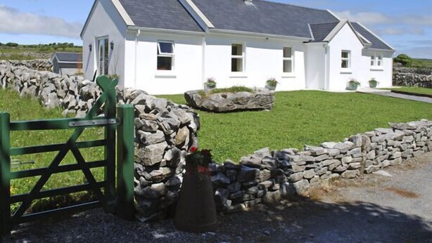 Una casa blanca con un muro de piedra y un portón verde.
