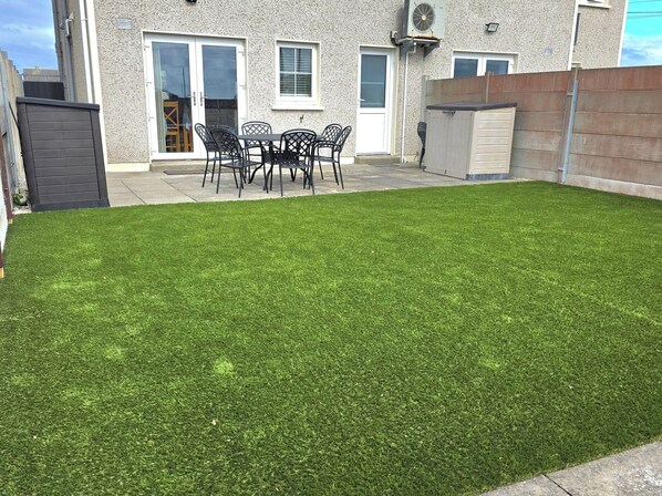 A backyard with artificial grass, a patio table with chairs, and a wooden fence.